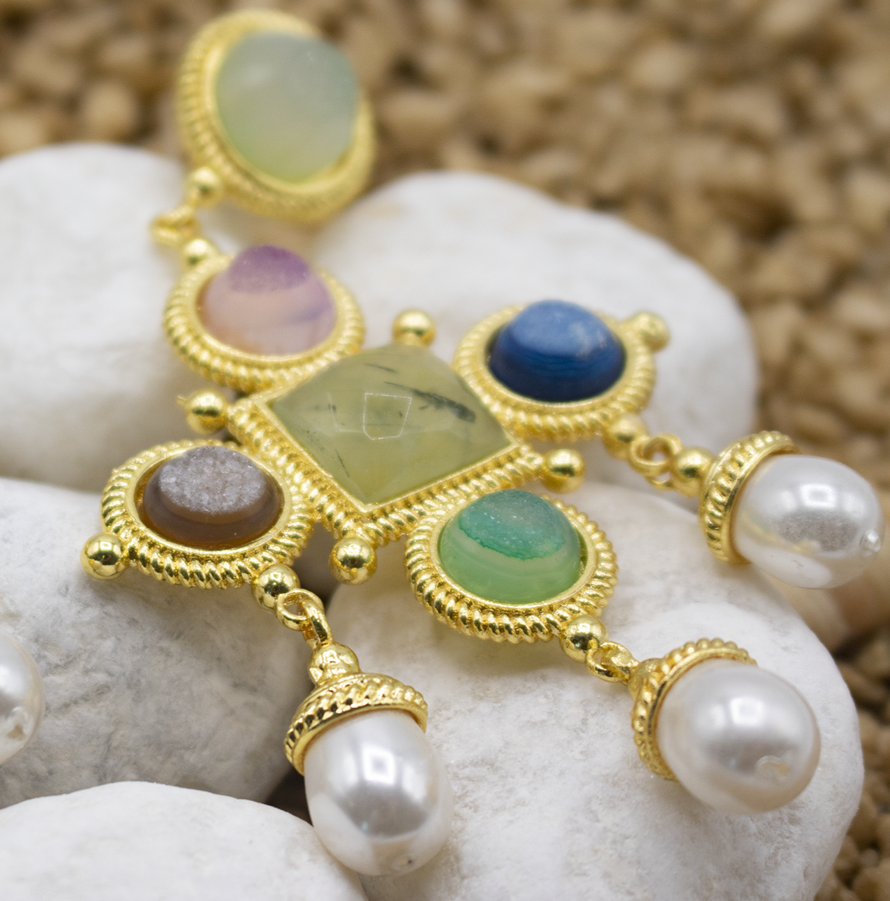 Pendientes largos piedras semipreciosas y perlas encima de piedras blancas y arena