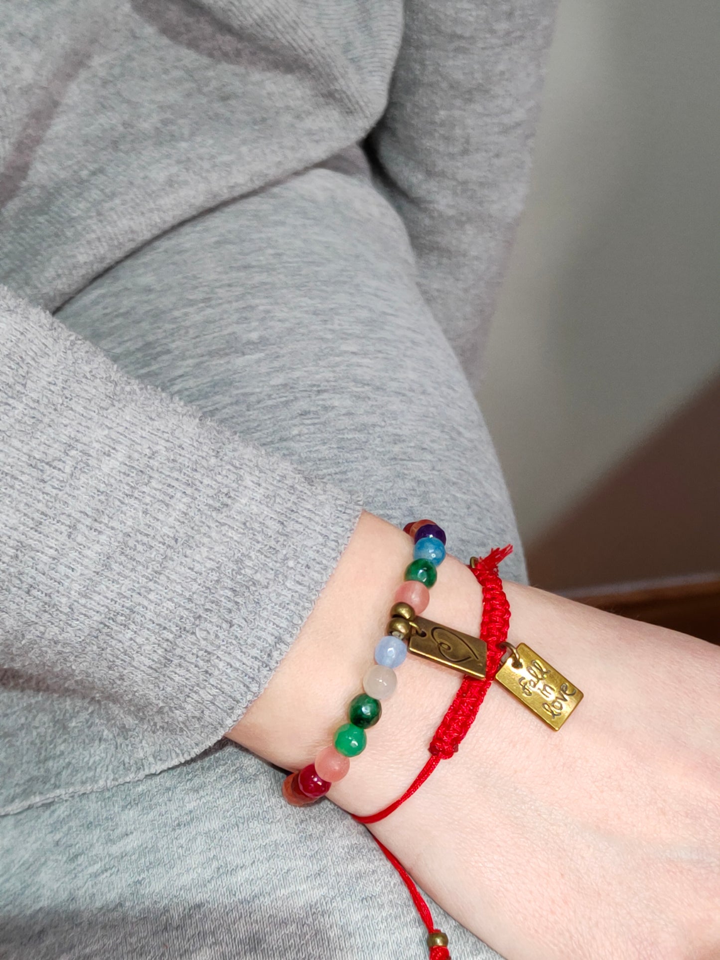 Pulsera de macramé roja con medalla corazon y borla roja y pulsera de bolas de colores con la misma medalla color bronce por la cara del mensaje "fall in love"