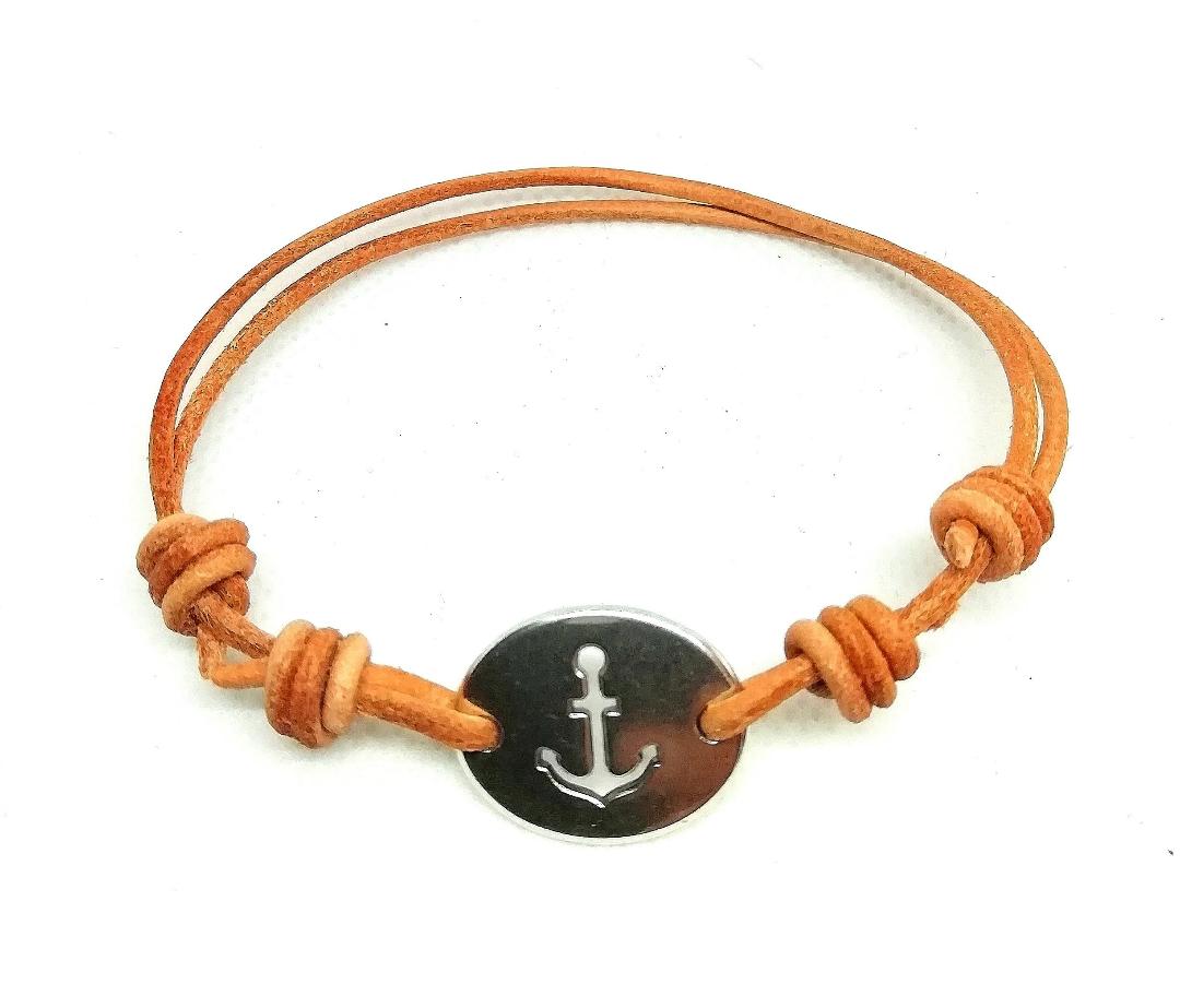 Pulsera de chapa metálica con ancla troquelada y cuero de color natural. Cierre de nudos corredizos adapatable.