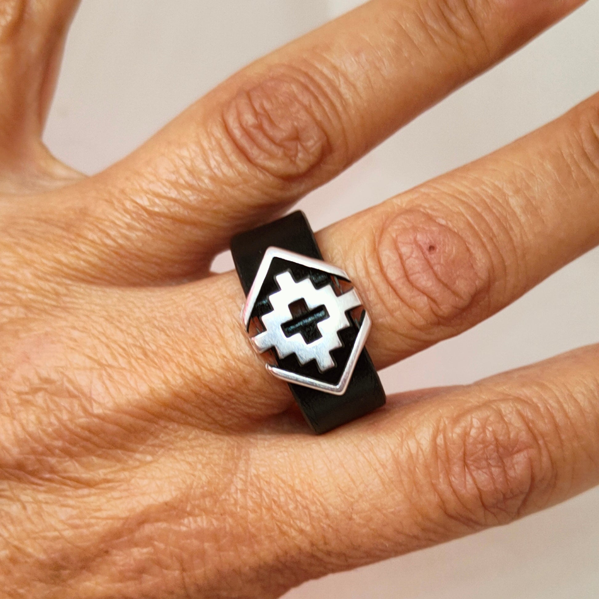 Anillo de cuero negro y pieza metálica geométrica puesto en dedo