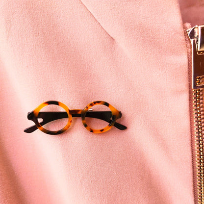 Broche gafas pasta  redondas con tonos marrones y beiges y patillas negras  puesto en cazadora