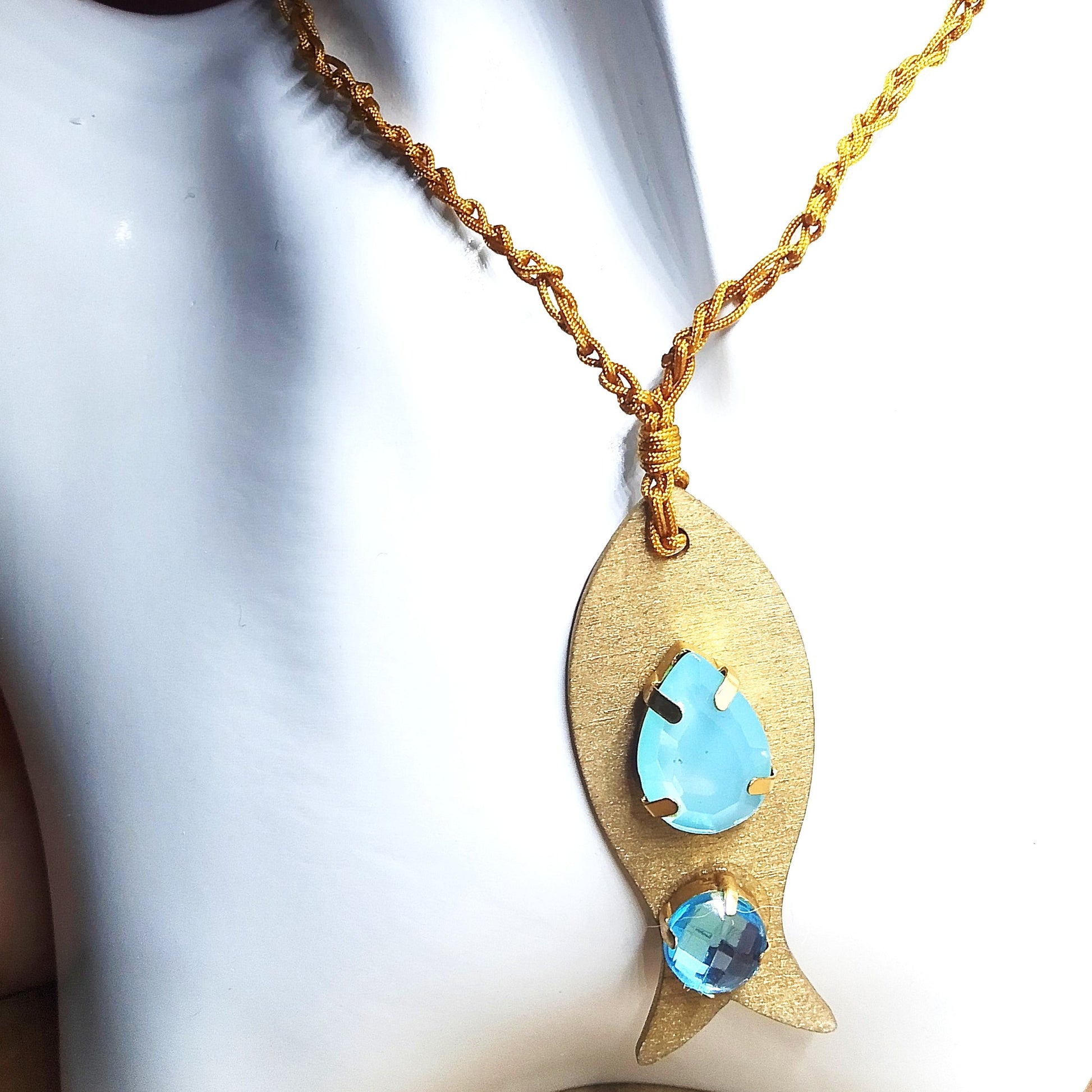 Pieza de collar en forma de pez de color dorado con piedras de bisutería con piedras azules en maniquí