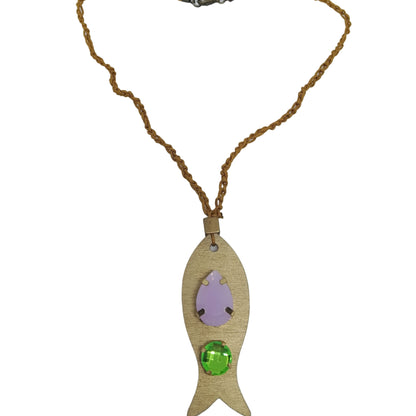 Pieza de collar en forma de pez de color dorado con piedras de bisutería con piedra verde y lavanda visto desde arriba