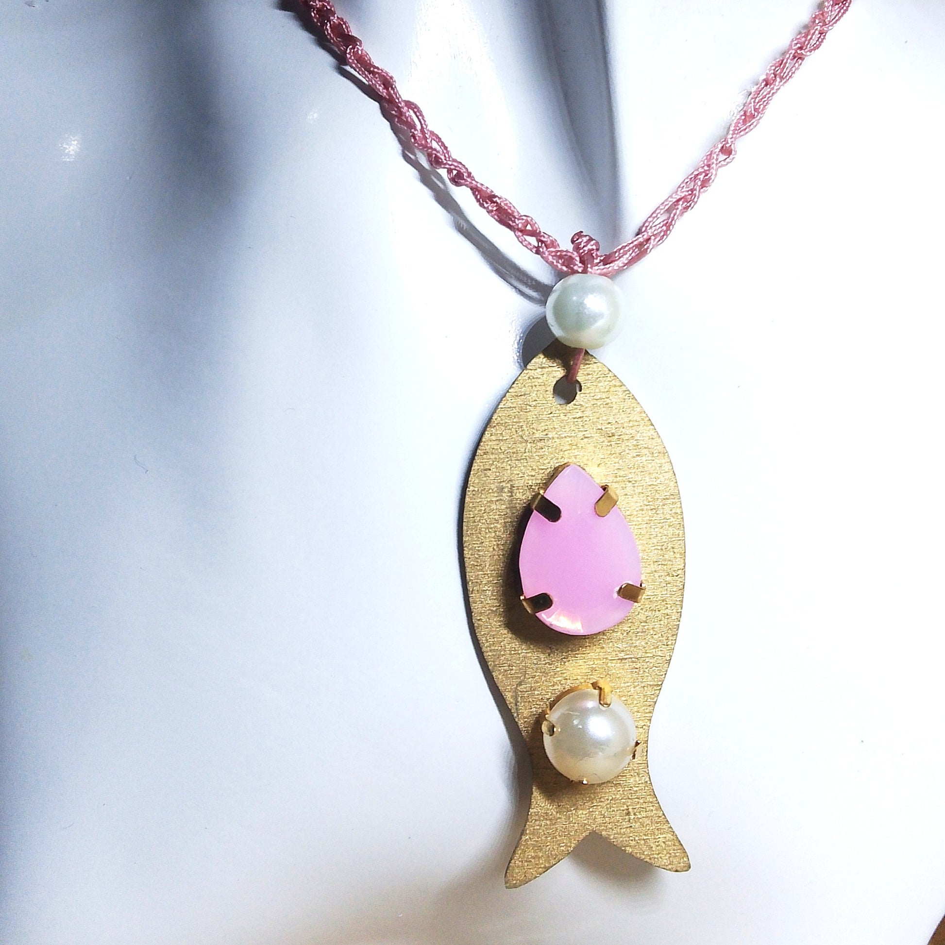Pieza de collar en forma de pez de color dorado con piedras de bisutería con piedra rosa y perla en maniquí